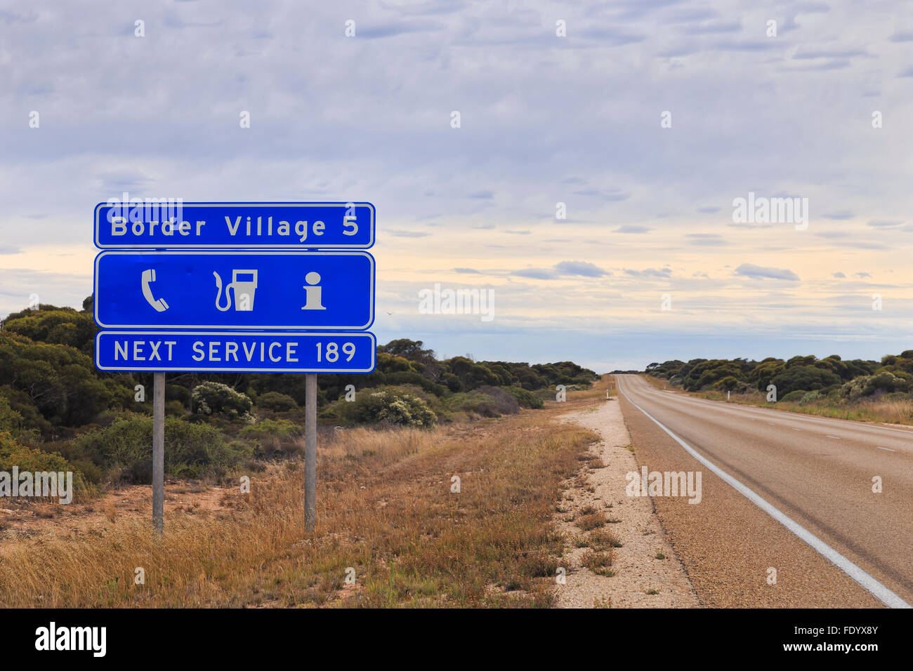 blaue informative Straßenschild in Westaustralien über nächsten Service sowie die Perspektive der Eyre Highway in Richtung Grenze Villa Stockfoto