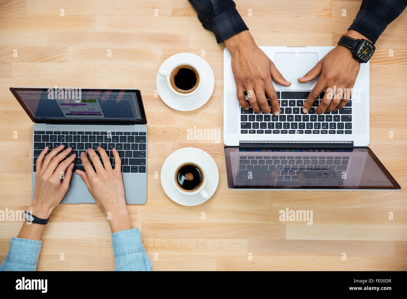 Draufsicht der Hände von Mann und Frau arbeiten mit zwei Laptops und Kaffeetrinken auf Holztisch Stockfoto