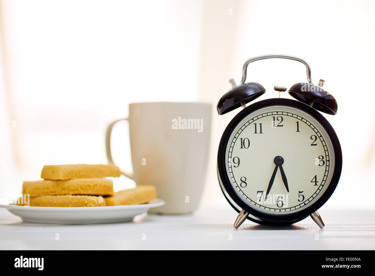Wecker und Frühstück am weißen Tisch Stockfoto