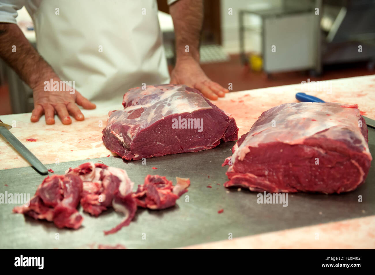 Nicht identifizierbare männliche Metzger ruht momentan zwischen großen Platten schneiden von rohem Fleisch mit Messern auf Tisch in der Lebensmittelverarbeitung Stockfoto