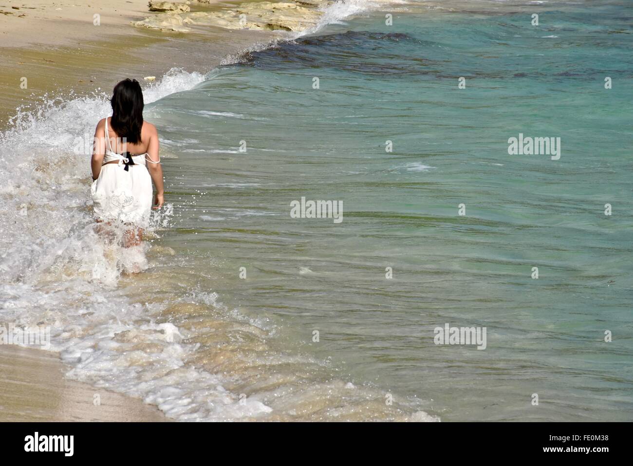 Frau im weißen Kleid zu Fuß in den tropischen Gewässern auf einem karibischen Strand. Stockfoto