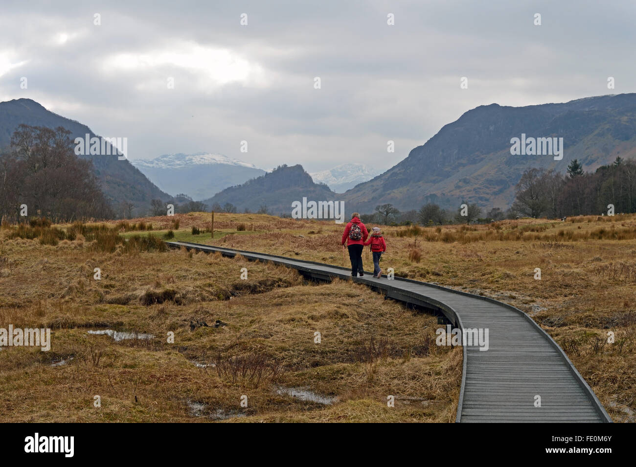 zwei Wanderer in roten Mäntel/Jacken in einer hügeligen/bergigen Landschaft schreiten Stockfoto