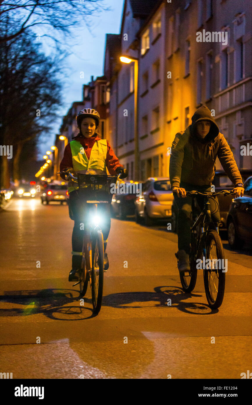 Radfahrer fahren, in der Dämmerung, in einer Stadtstraße, mit und ohne Beleuchtung und Sicherheitskleidung, Fahrrad Sicherheit, Sichtbarkeit bei Nacht Stockfoto