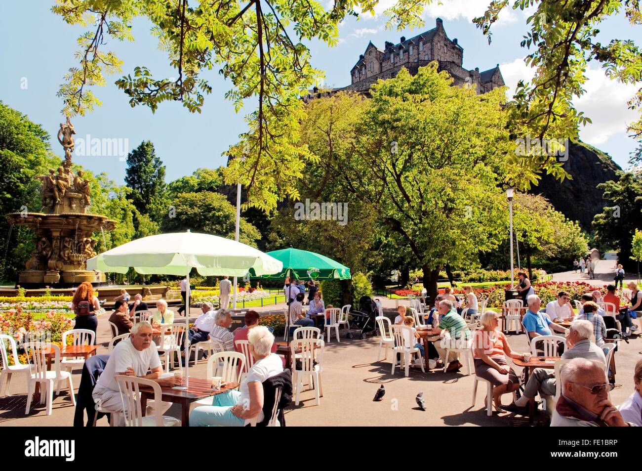 Edinburgh Castle erhebt sich hinter dem Café und der Ross Fountain in Princes Street Gardens, Edinburgh, Schottland, Vereinigtes Königreich. Sommer Stockfoto