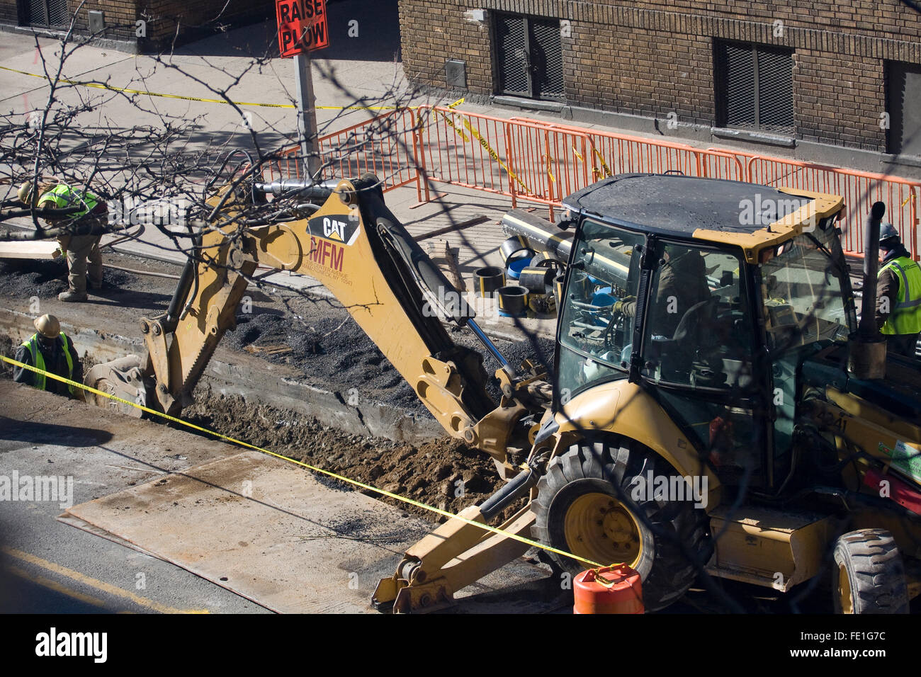 Bauarbeiter stehen in einem Graben wie ein gelber Bagger von Caterpillar gemacht einen Graben in einer New Yorker Straße Graben ist Stockfoto