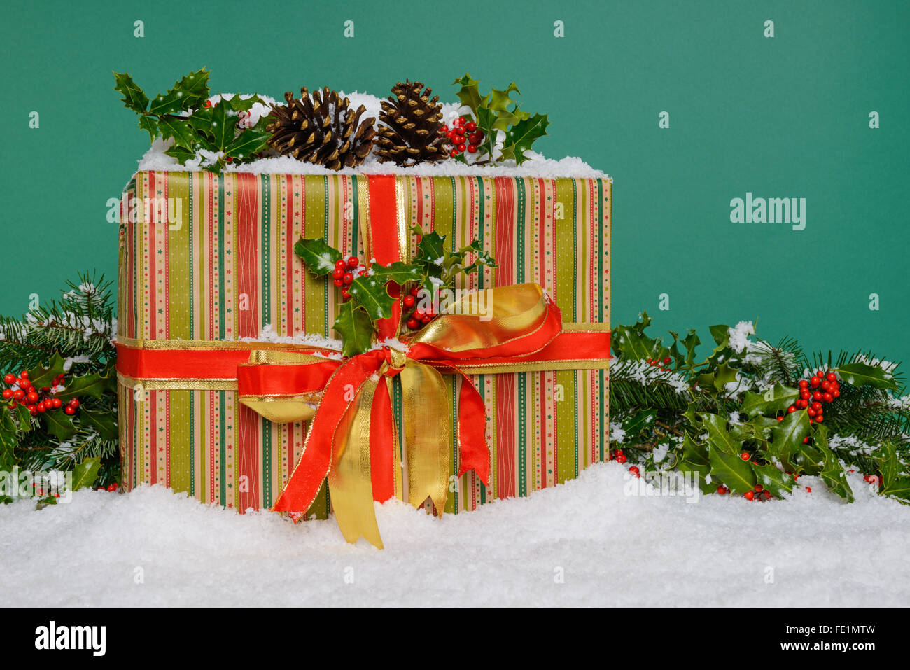 Ein Geschenk verpackt Weihnachtsgeschenk von einem holly Garland und Schnee, grünen Hintergrund umgeben. Stockfoto