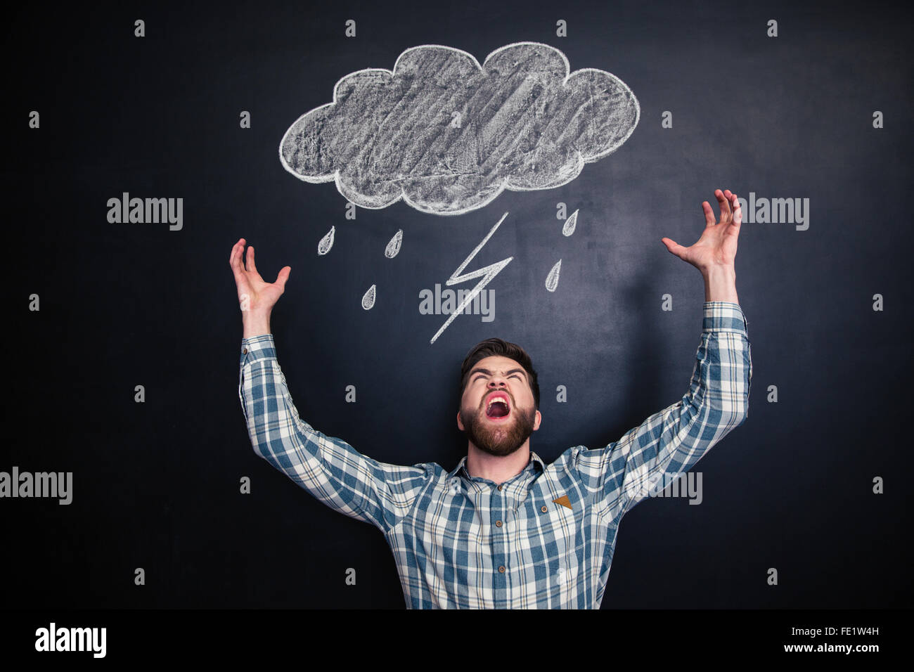 Zorniger junger Mann mit Bart mit erhobenen Händen stehen und schreien über Tafel mit gezeichneten Regenwolke Stockfoto