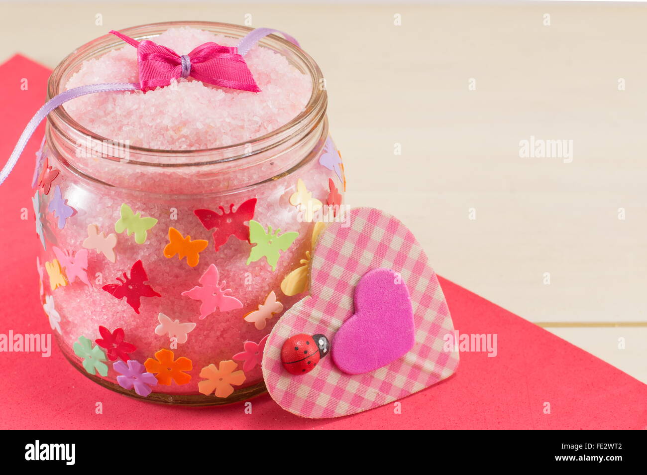 Badesalz in einem Glas neben einem rosa karierten Herz-symbol Stockfoto