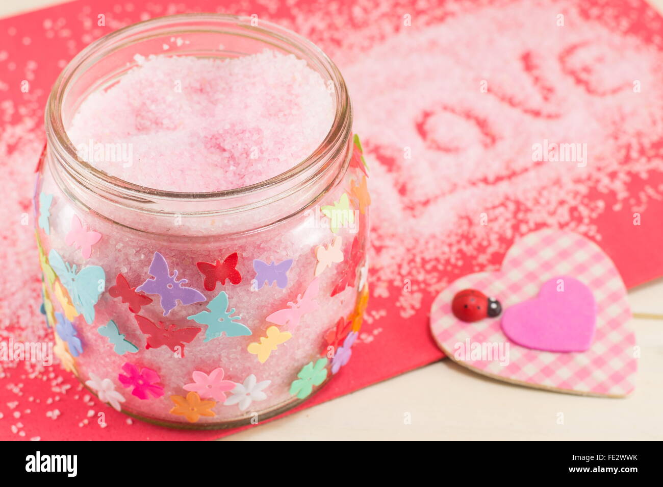 Badesalz in einem Glas neben einem rosa karierten Herz-symbol Stockfoto