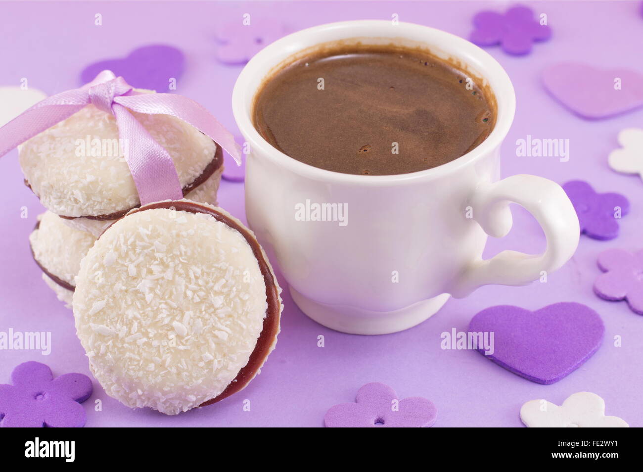 Weiße Tasse Kaffee mit Dessert auf einem lila gedeckten Tisch Stockfoto