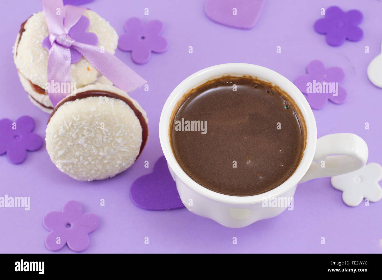 Weiße Tasse Kaffee mit Dessert auf einem lila gedeckten Tisch Stockfoto