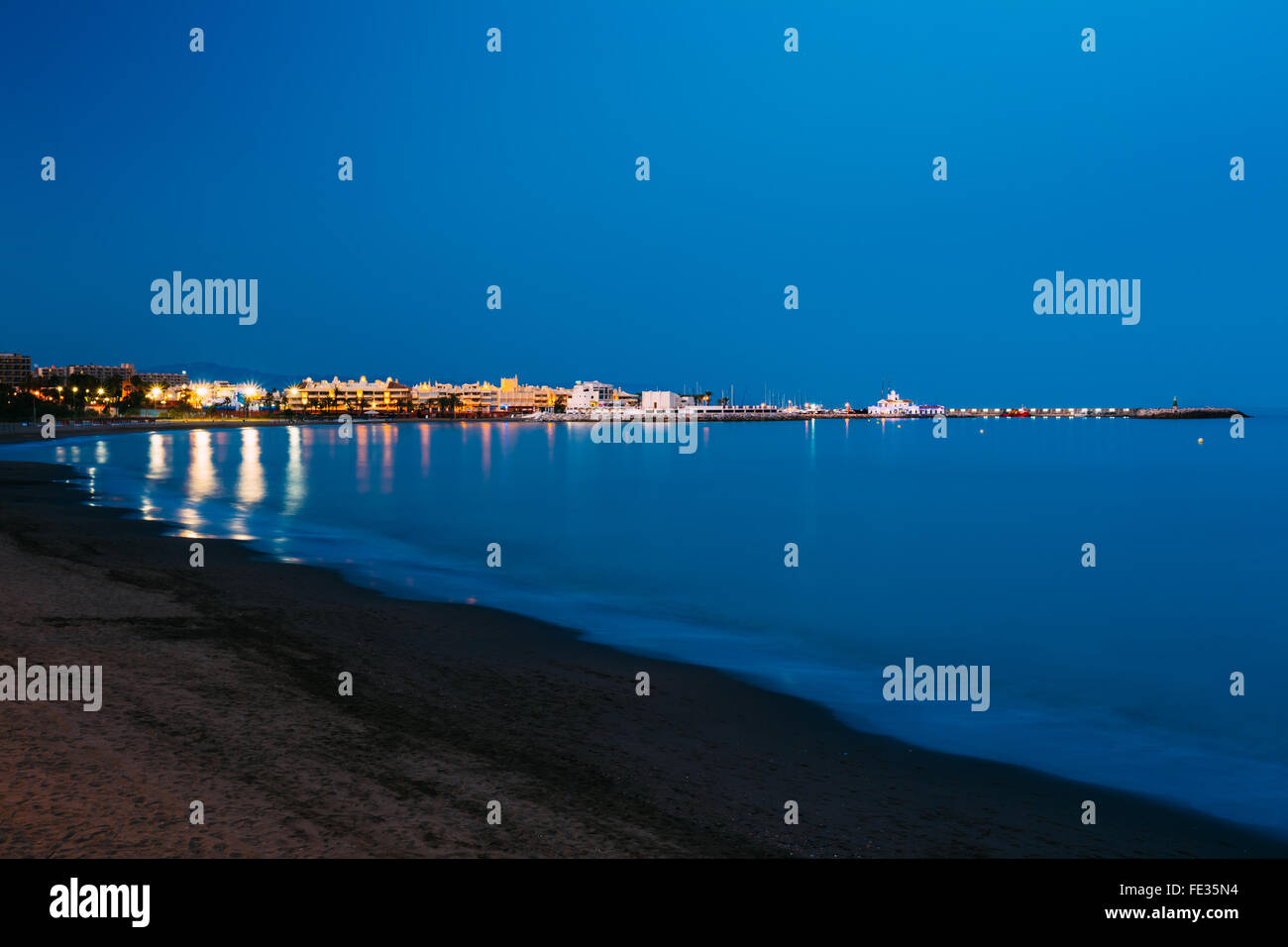 Nacht szenische Ansicht der verlassene Strand, Seeküste und leuchtende Benalmadena entfernt. Ruhiges Meer, tiefblaue Meerwasser und Himmel. Spanien. Stockfoto