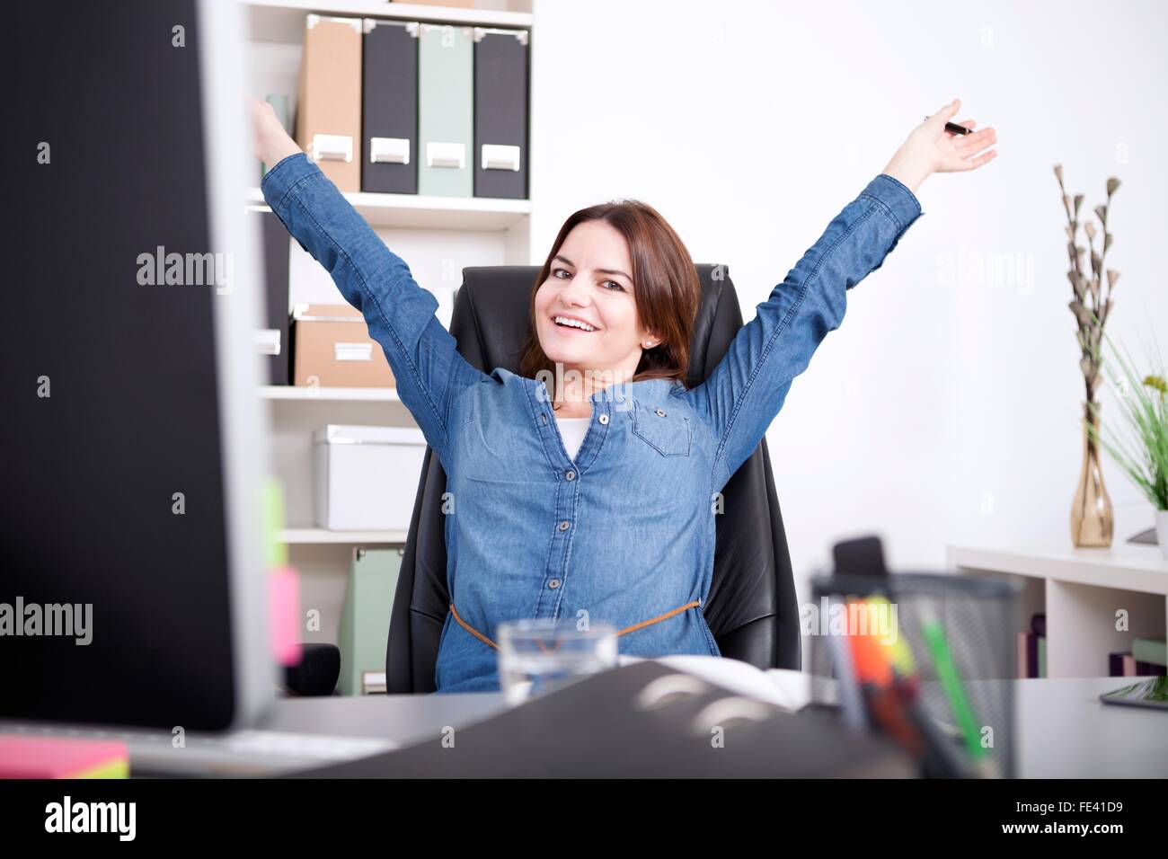 Glücklich weibliche Executive sitzt auf ihrem Stuhl im Büro und streckte ihre Arme und Looking in die Kamera. Stockfoto