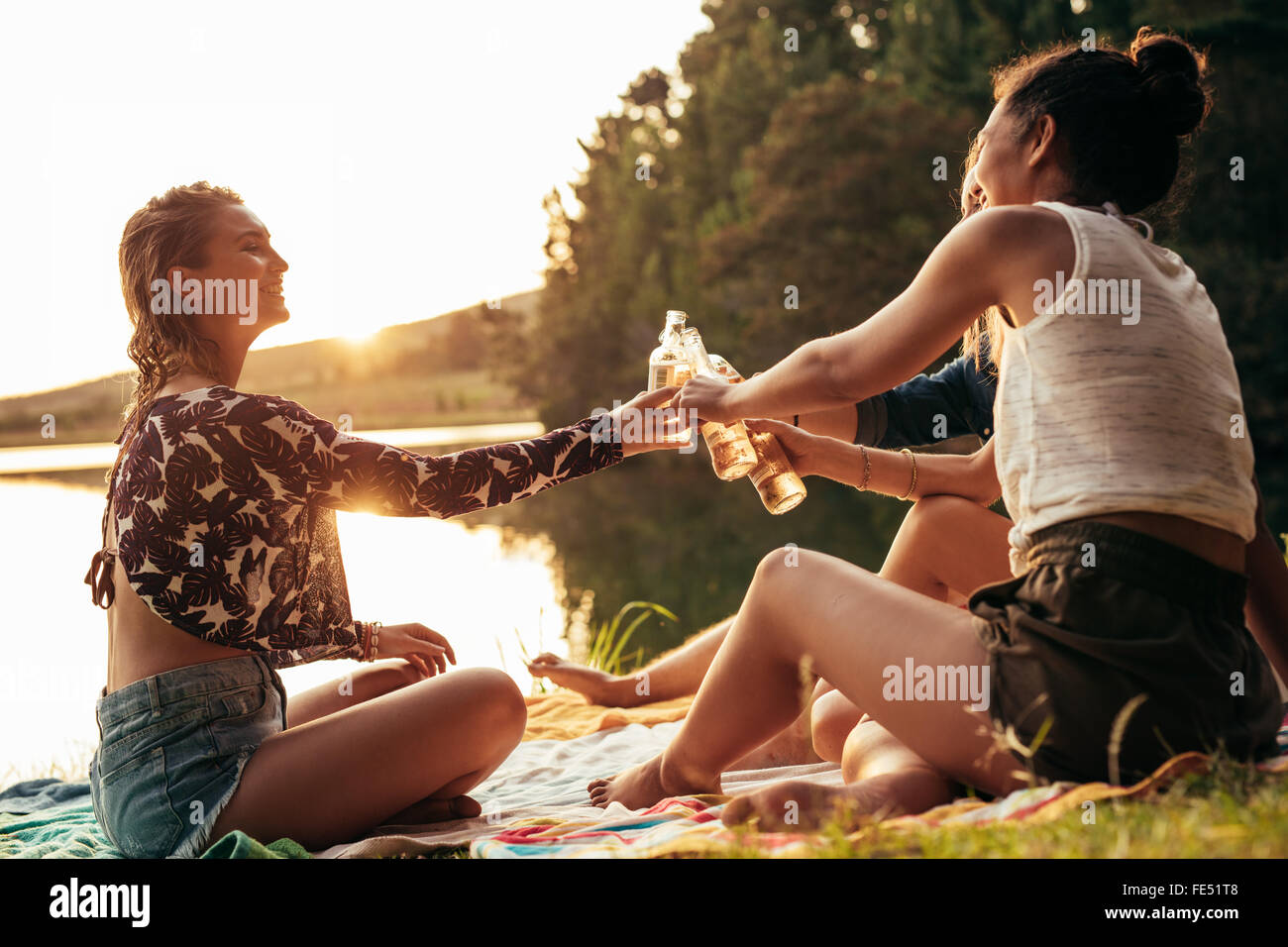 Gruppe junger Frauen, die an einem See zu feiern. Junge Freunde sind einander mit Bier während des Sonnenuntergangs am See toasten. Stockfoto