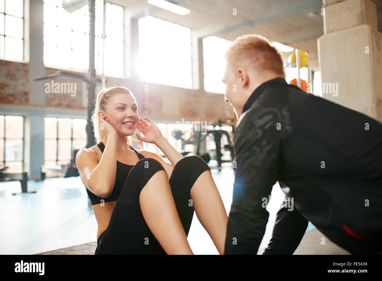 Innenaufnahme einer jungen Frau Sit während ein personal Trainer hält ihre Füße. Glücklich weiblich abs Übung mit Hilfe Stockfoto