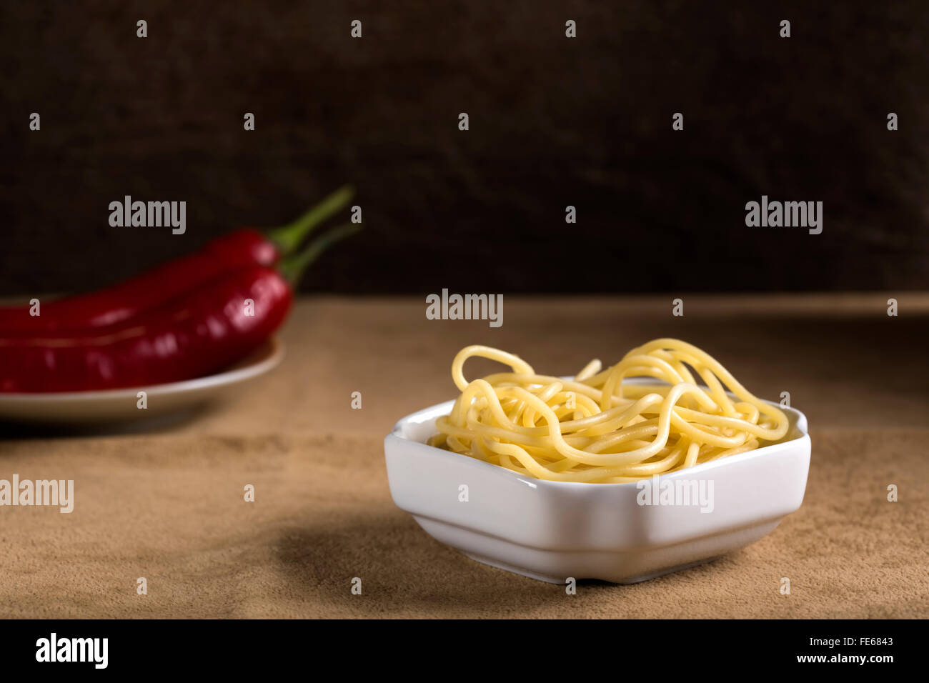Gekochte Spaghetti in weißer Schale und roten Peperoni im Hintergrund Stockfoto