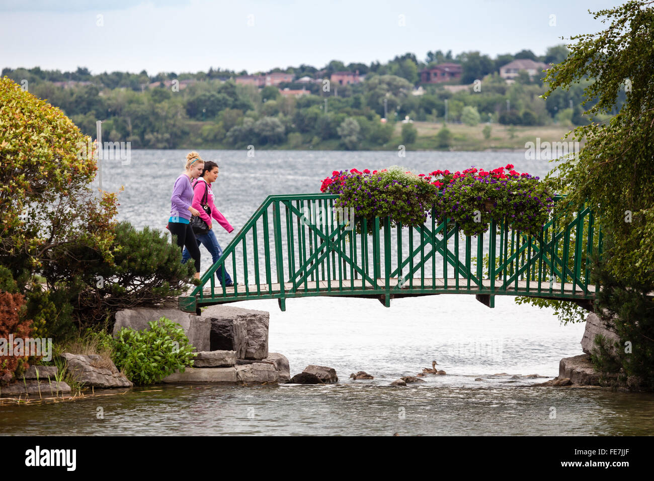 Zwei Damen gehen zügig über eine Brücke mit großen Blumenkästen mit See im Hintergrund. Stockfoto