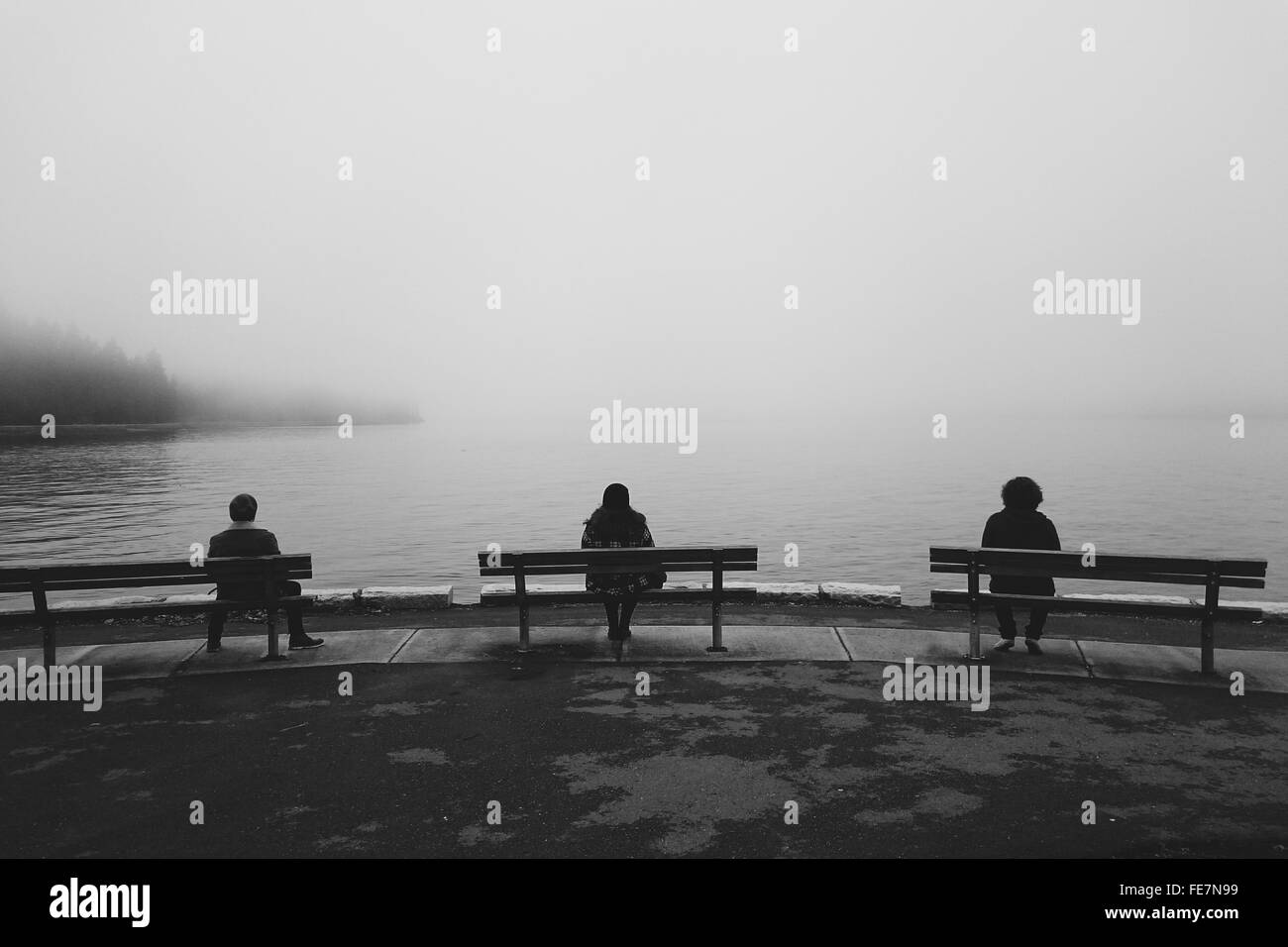Drei Leute sitzen auf den Bänken am Seeufer Stockfoto