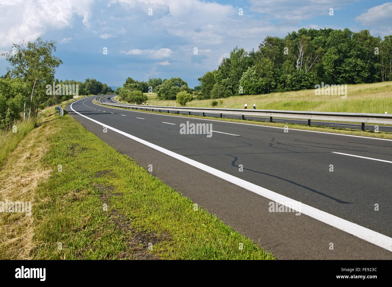 Leere Autobahn, vorbei an romantischen Landschaft, in der Ferne ein Auto, Wiesen und Bäumen, die durch den Wind, dramatische Wolken, Linie VI gebogen Stockfoto