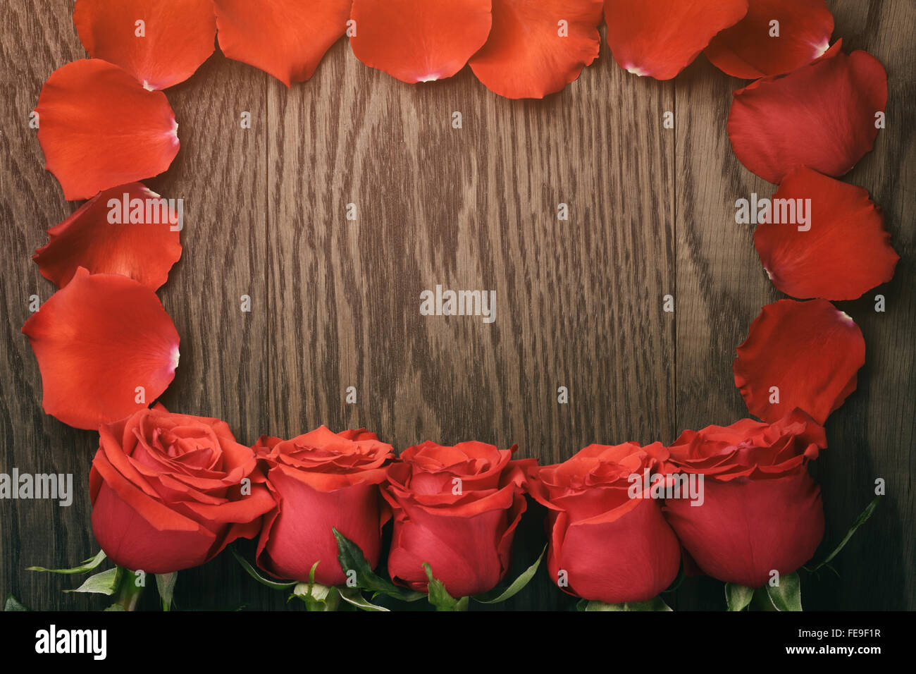 Komposition mit dunklen roten Rosen in einer Reihe auf Holztisch Stockfoto