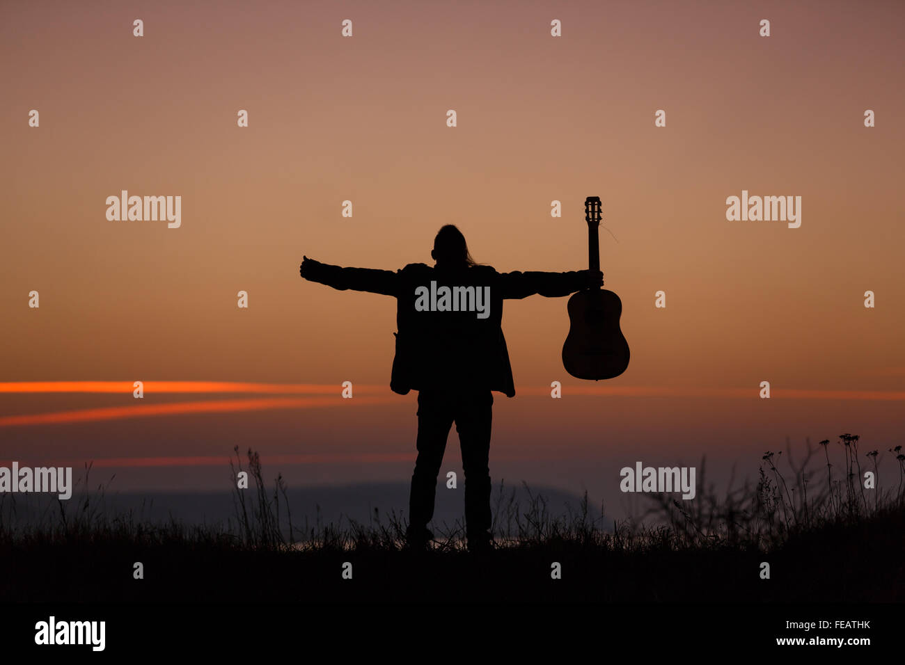 Mann, stehend mit Gitarre im Sonnenuntergang Stockfoto