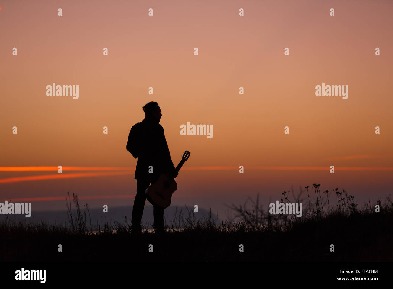 Mann, stehend mit Gitarre im Sonnenuntergang Stockfoto