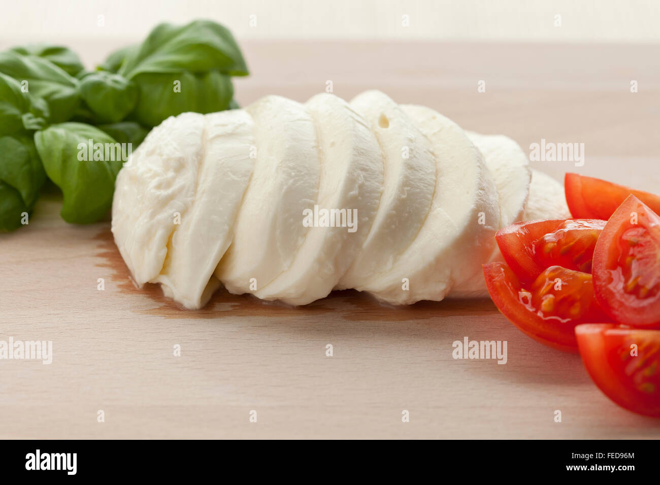 Frischer Mozzarella-Scheiben mit Basilikum und Tomaten auf Holzbrett Stockfoto