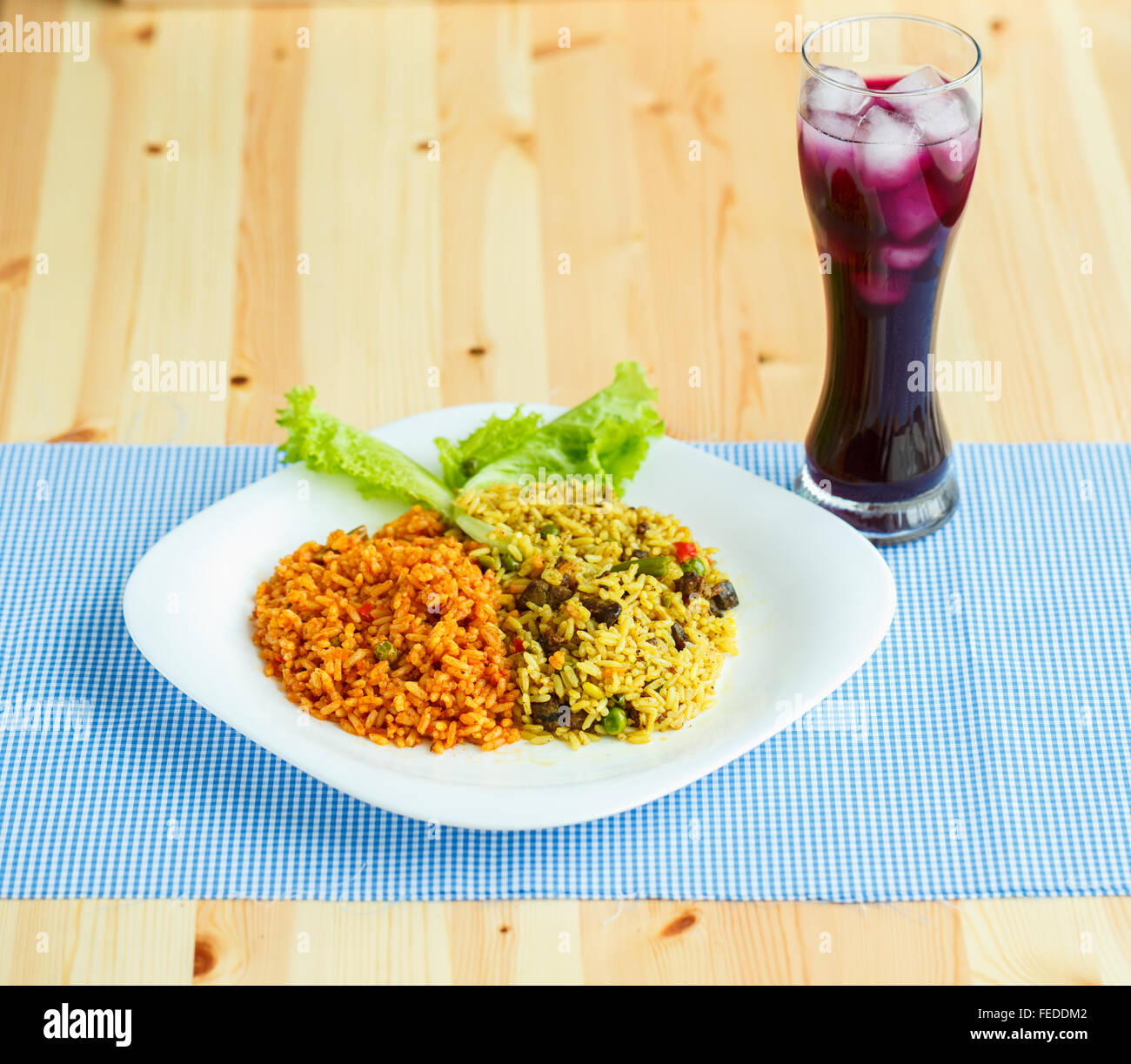 Leckere Gericht aus zwei Arten von Reis auf einem weißen Teller und ein Glas Saft mit Eis Stockfoto