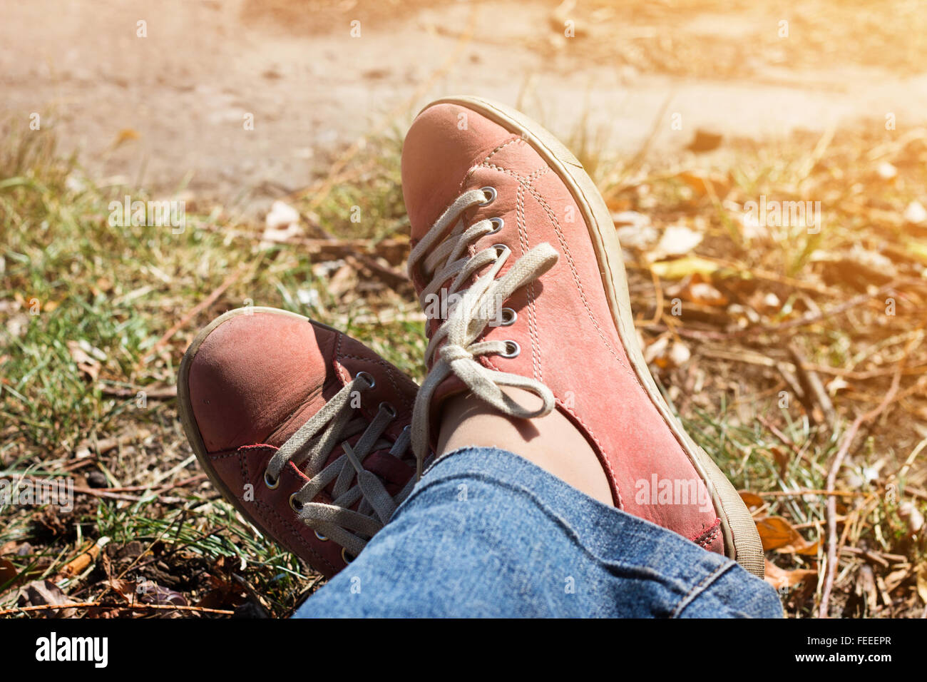 Beine gekreuzt in rote Turnschuhe und Jeans im Freien. Entspannen Sie im Herbst Park. Stockfoto