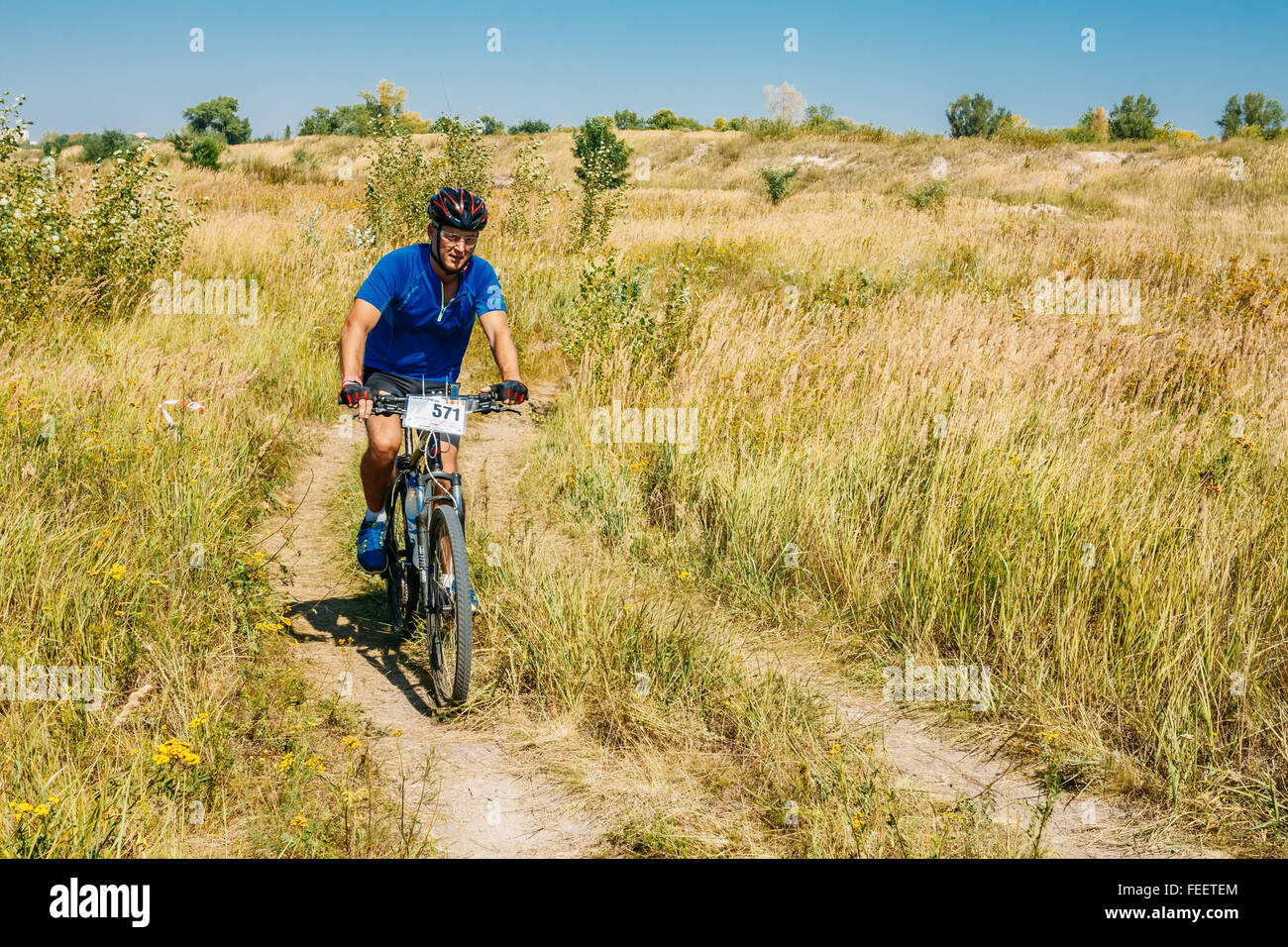 Mountain Bike Radfahrer Mann Reiten Track auf gelbe Wiese am sonnigen Tag. Aktiver Sport, gesunde Lebensweise, Wettbewerb zu üben. Stockfoto