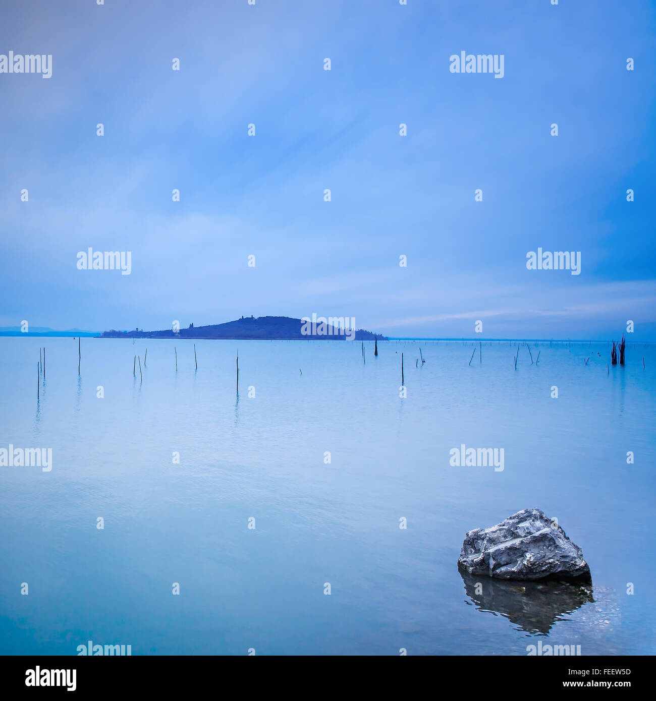 Wasseroberfläche, Polen, Island und Rock in einem blauen Morgen am Trasimeno See, Umbrien Italien Europa. Hügel im Hintergrund. Stockfoto