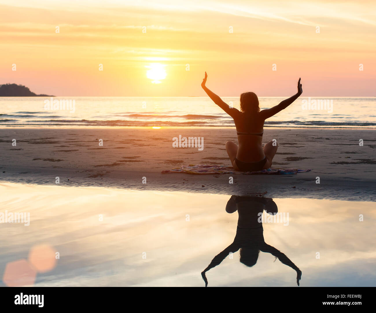 Yoga-Silhouette der Frau Übung bei Sonnenuntergang am Strand mit Spiegelbild im Wasser. Stockfoto