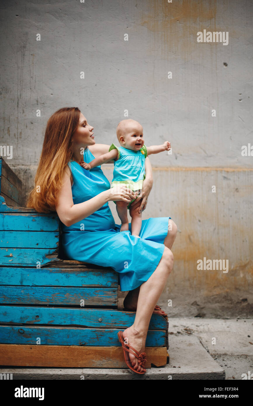 Cute 1 Jahr Baby stehend auf Mutters Knie. Familie Kleidungsstil mit blauen Farben. Selektiven Fokus auf Mutter. Stockfoto