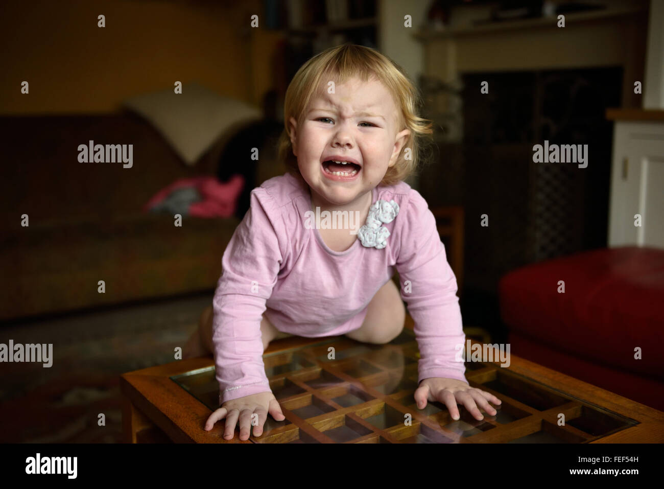 Ein unglücklich achtzehn Monate altes Baby mit einer Temperatur knelling einem Beistelltisch in ihrem Haus weint und sucht unglücklich. Stockfoto