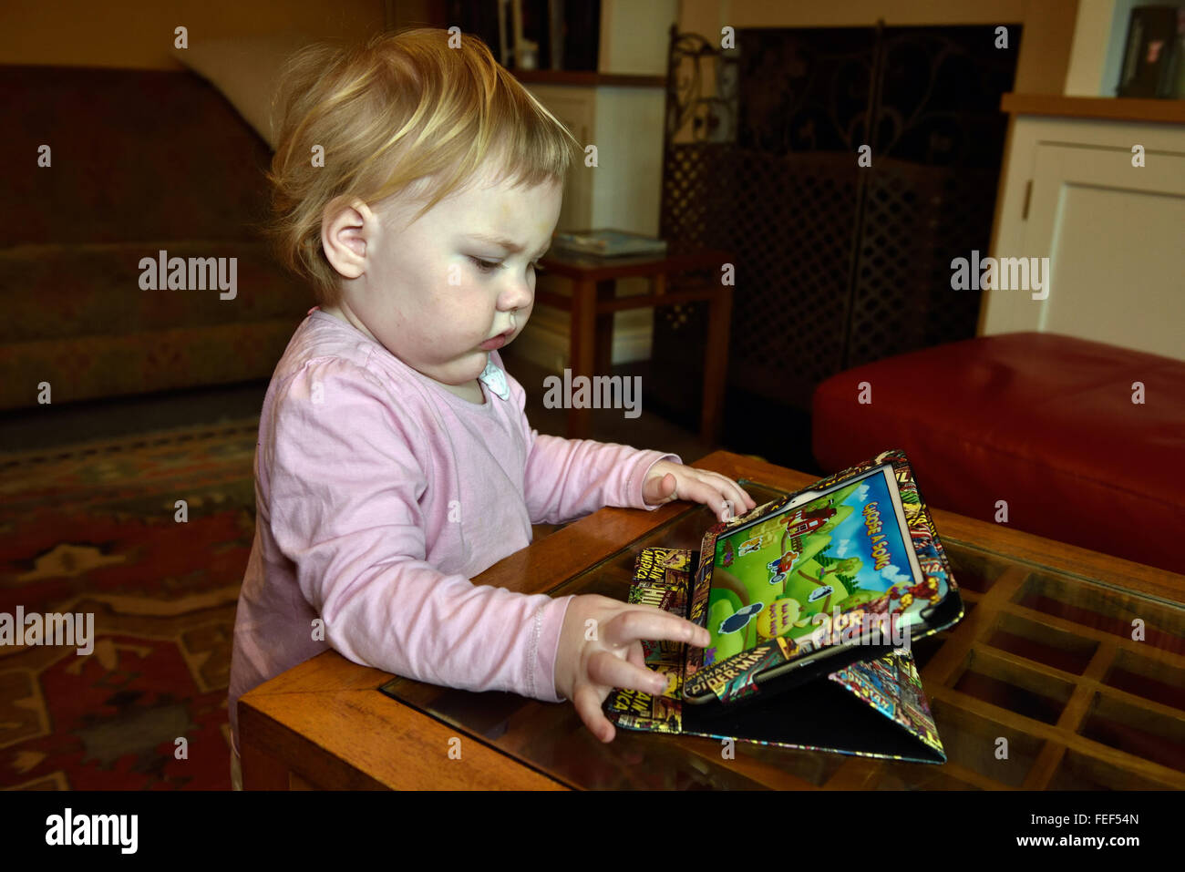 Ein 18 Monate altes Kleinkind Konzentration während des Spiels auf einem Ipad in ihrem Haus. Stockfoto