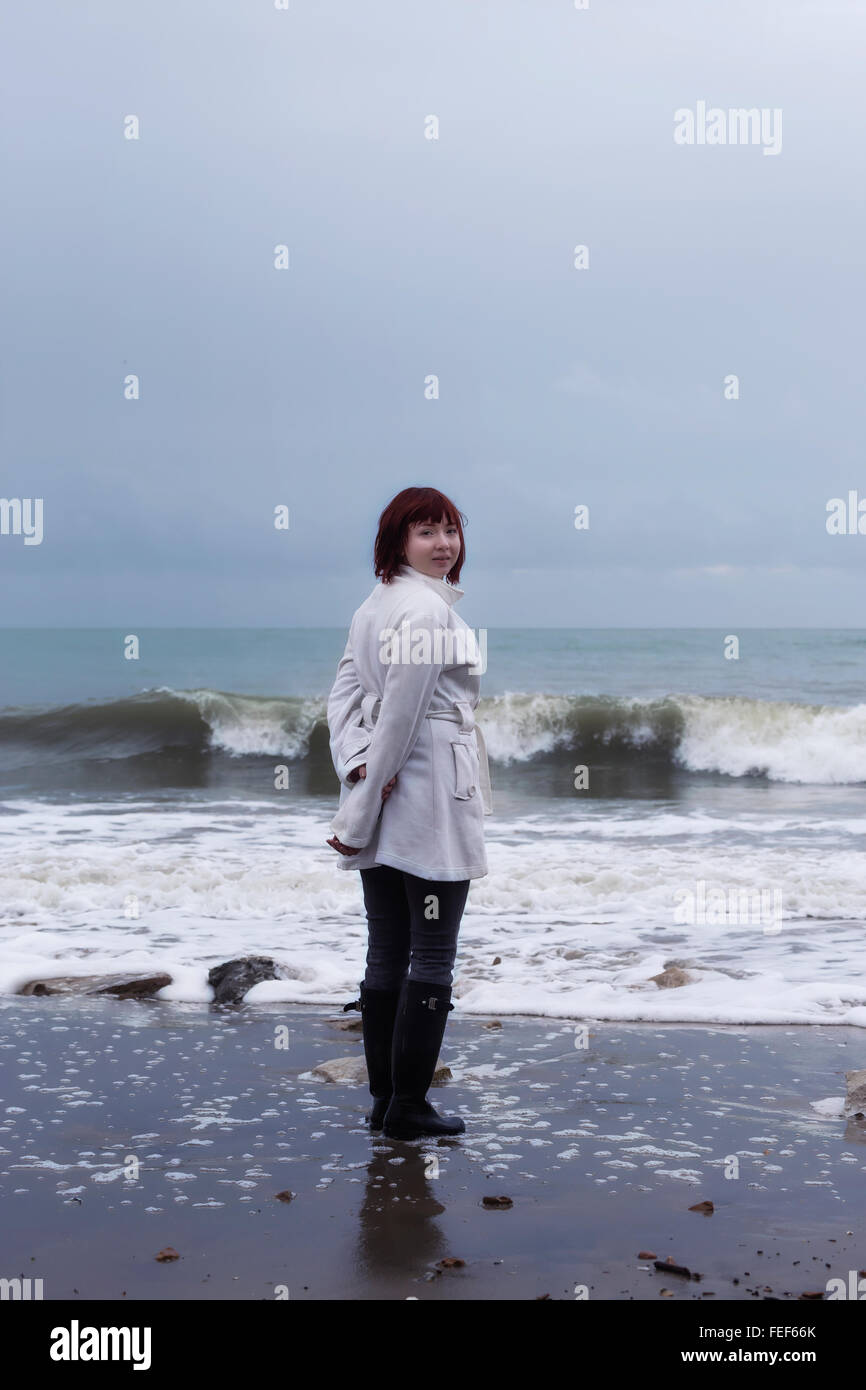 eine Frau in einem weißen Kittel steht am Meer im winter Stockfoto