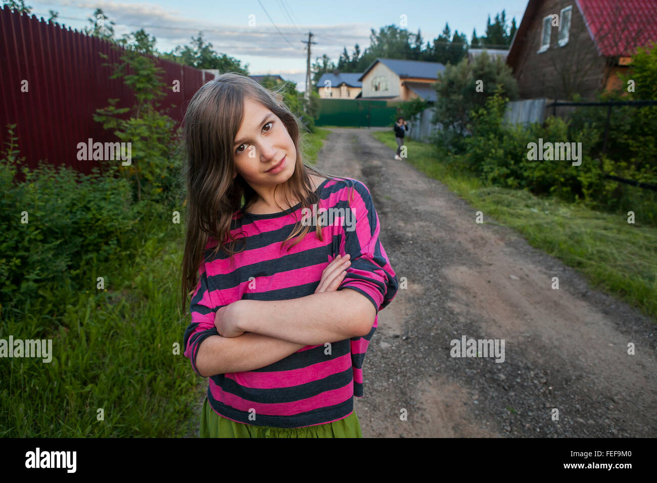Lächeln Teenager-Mädchen in einem roten gestreiftes Hemd steht auf der Straße zwischen den Häusern, verschränkte ihre Arme über der Brust. Stockfoto