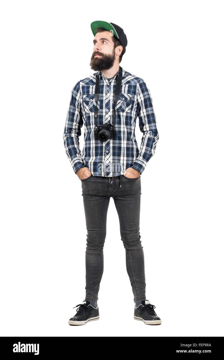 Entspannte Hipster tragen schwarze Dslr-Kamera über Hals mit Händen in den Taschen. Ganzkörper-Länge-Porträt über weißen isoliert Stockfoto