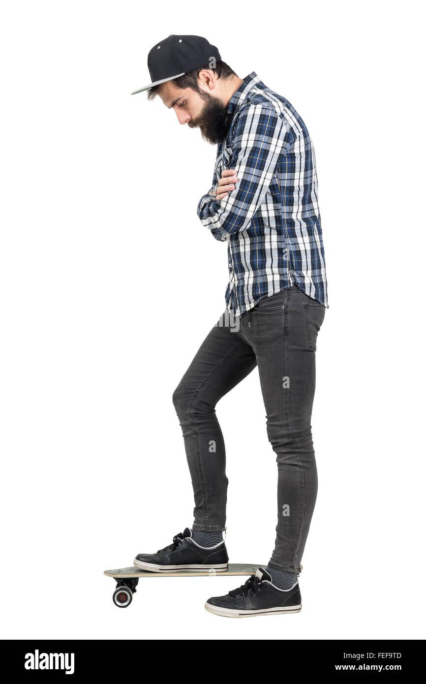 Hipster mit verschränkten Armen nach unten stehend auf Skateboard. Seitenansicht. Ganzkörper-Länge-Porträt über weißen isoliert Stockfoto