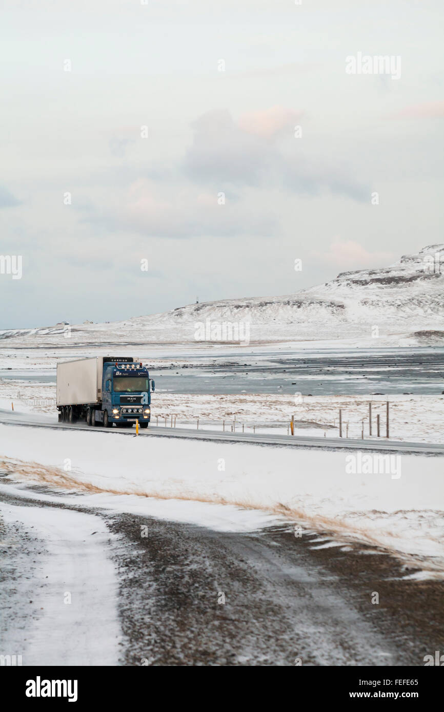 Lkw Fahren entlang der Straße durch schneebedeckte Berge in Island im Februar Stockfoto