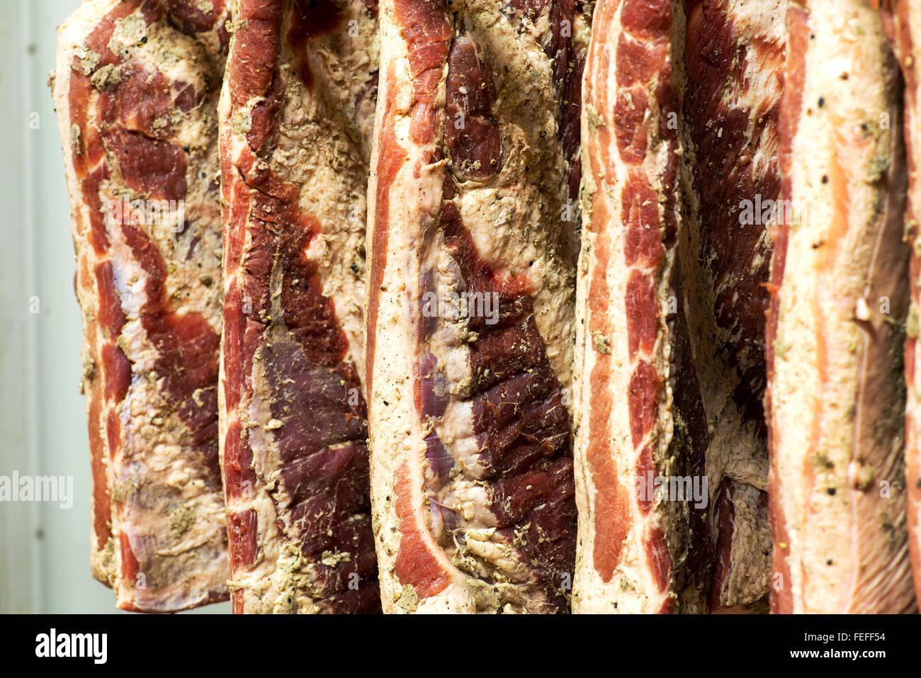 Full-Frameansicht von unbeschnittenen Seiten geräucherter Speck hängen an Haken in einer Metzgerei während des Alterungsprozesses Stockfoto