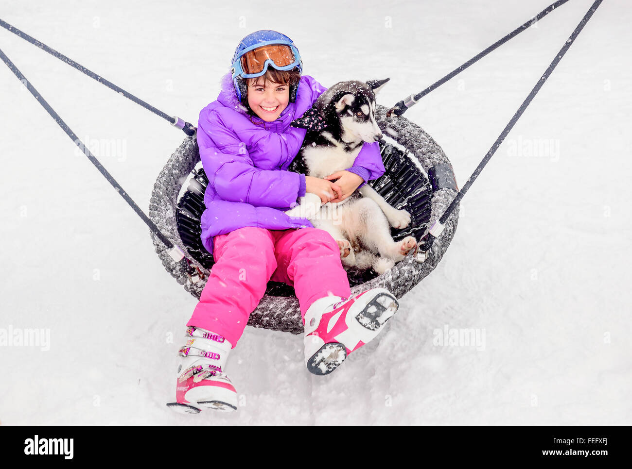 Glückliche kleine Mädchen sitzen auf der Schaukel mit husky Welpen Hund im winter Stockfoto