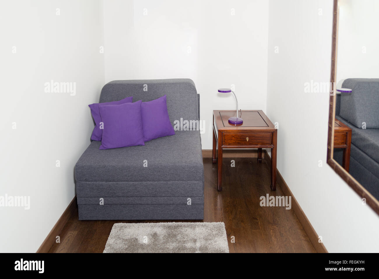 Bequeme Gray Sessel mit lila Kissen in der Nähe einen kleinen Tisch mit modernen Lampe. Sessel in einem kleinen Zimmer für die Gäste Erholung mit Stockfoto
