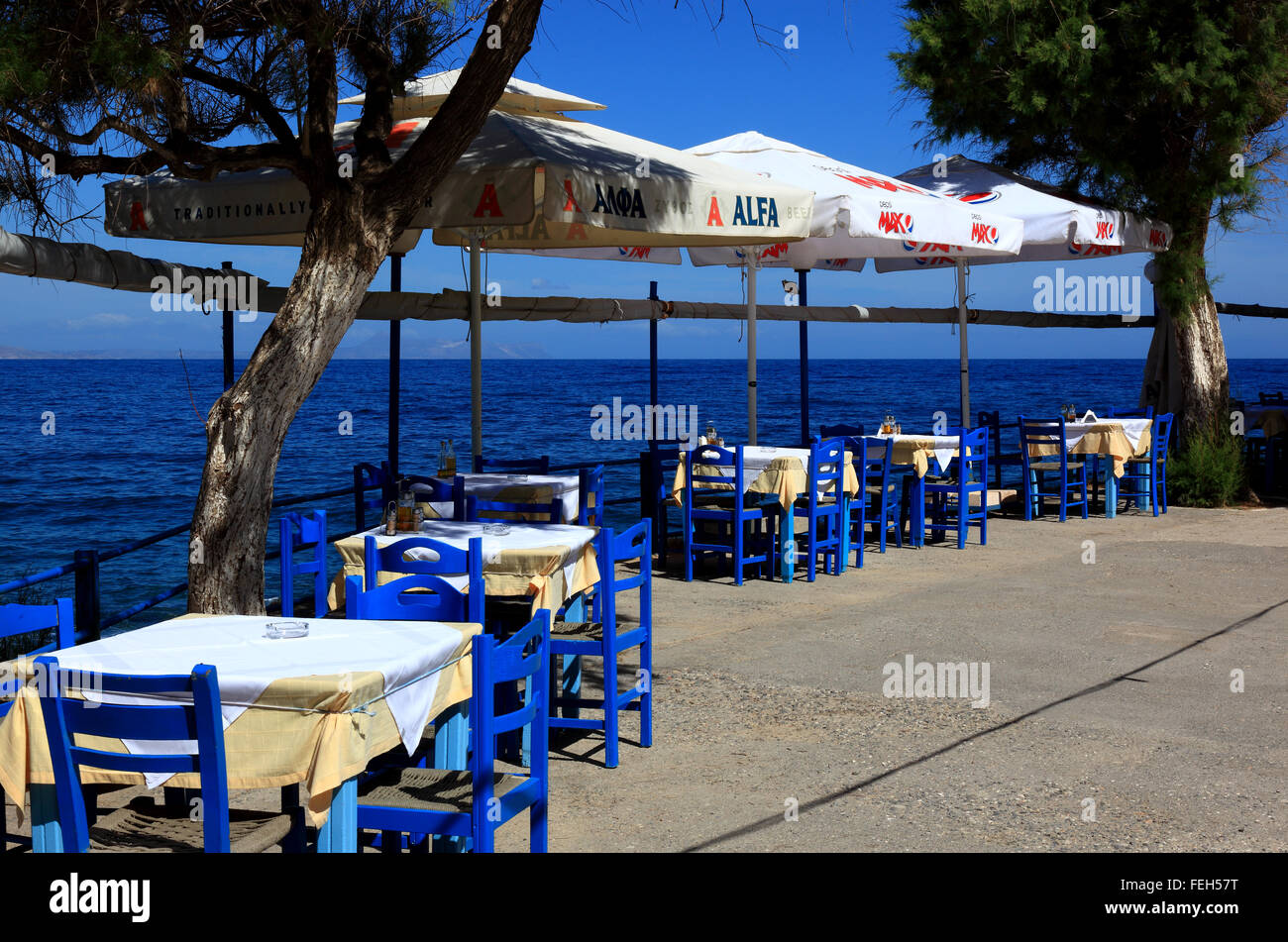 Kreta, Rethymnon, Straße Restaurant mit Blick auf das Meer, blaue Stühle, Tische und Sonnenschirme Stockfoto