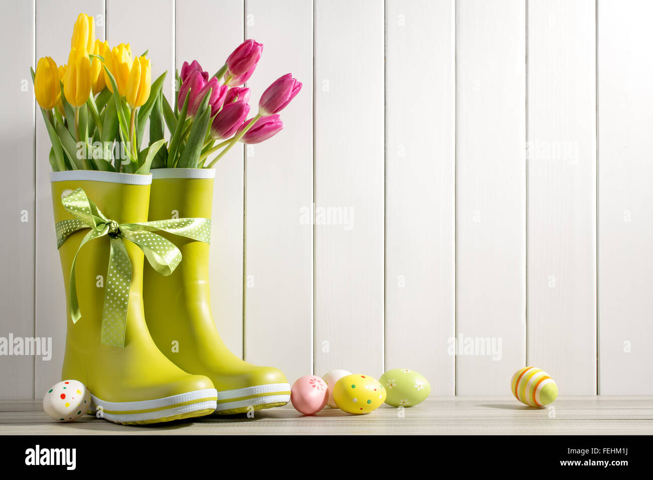 Regenstiefel, frische Tulpen und Ostereier auf Holz Hintergrund Stockfoto