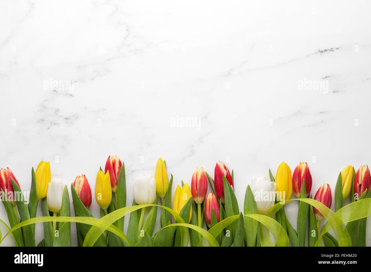 Tulpen mit Band auf weißem Marmor, Oster-Deko. Stockfoto