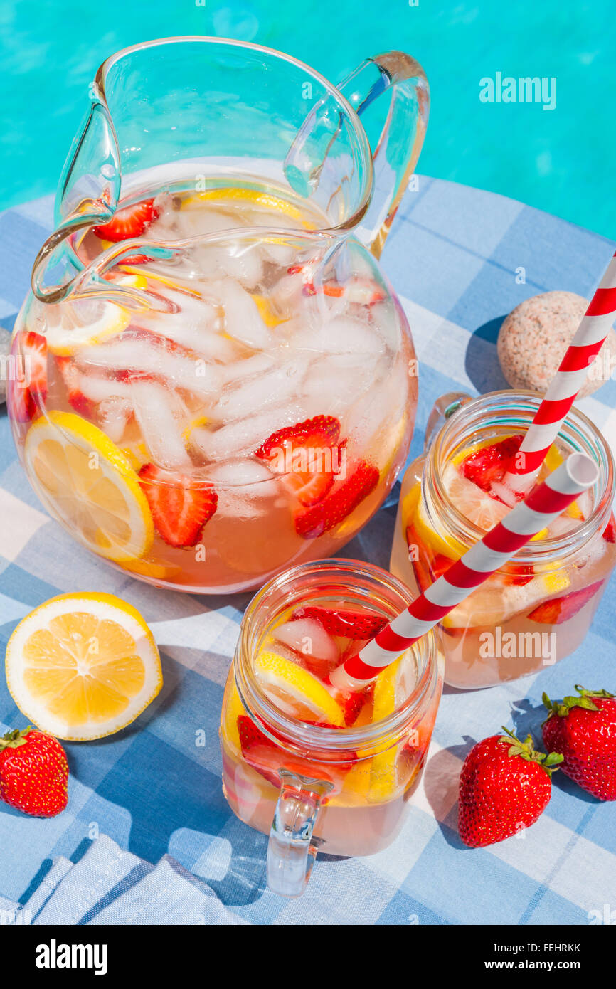 Eis kalt hausgemachte Erdbeer Limonade in Karaffe und Gläser mit Papier Strohhalme Beistelltisch Außenpool im Sommer Stockfoto