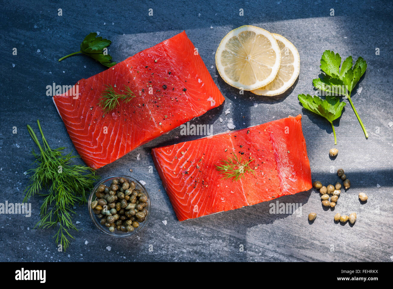 Zwei Stücke von roher Wilder Lachs Fisch Steaks mit Zitrone, Kapern und Kräutern, bereit, von oben zu kochen. Stockfoto
