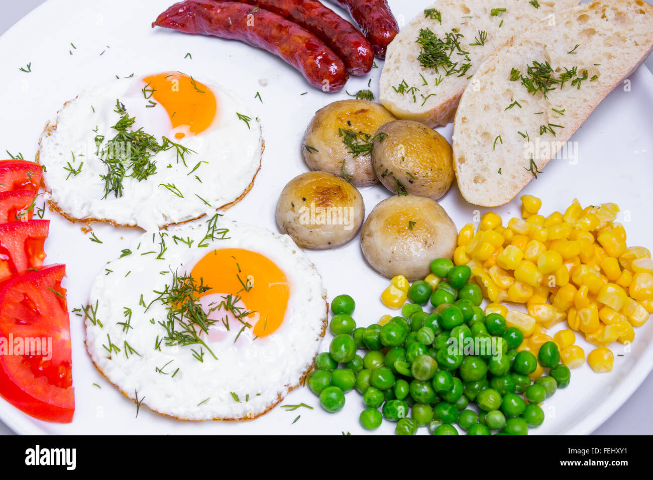 Reichhaltiges Frühstück mit Rührei, Würstchen und Gemüse in großen weißen Teller Stockfoto