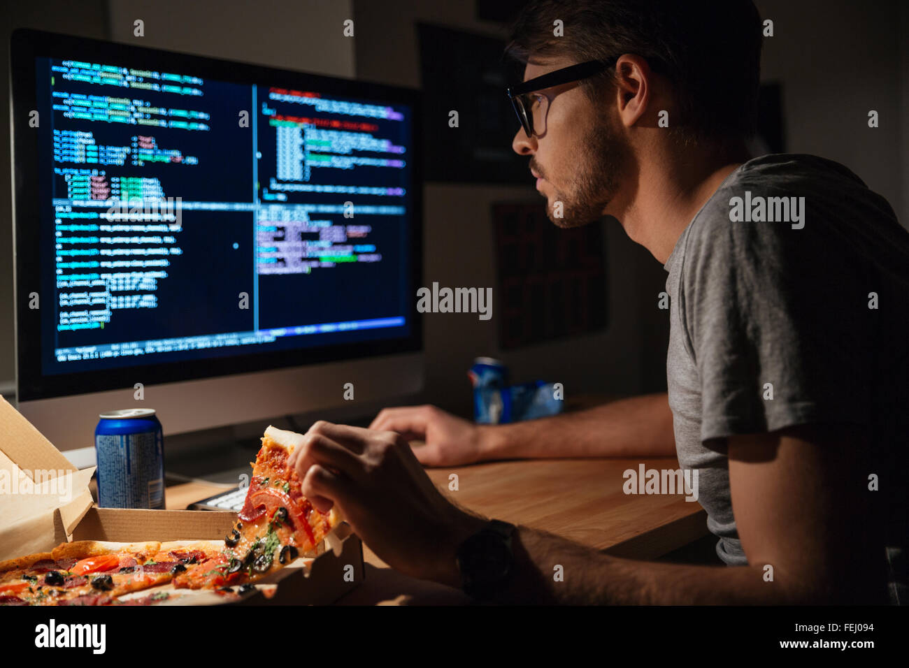 Profil von konzentrierten jungen Softwareentwickler Pizza essen und Codierung zu Hause Stockfoto